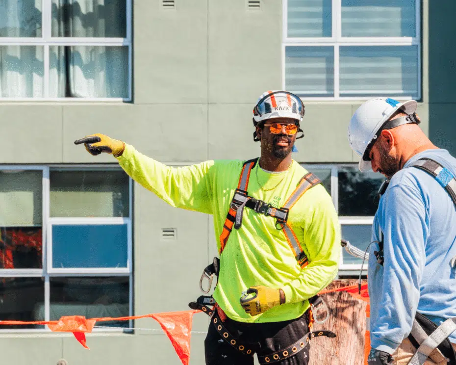 An installer in a high-visibility shirt pointing while briefing a colleague in front of an apartment building.