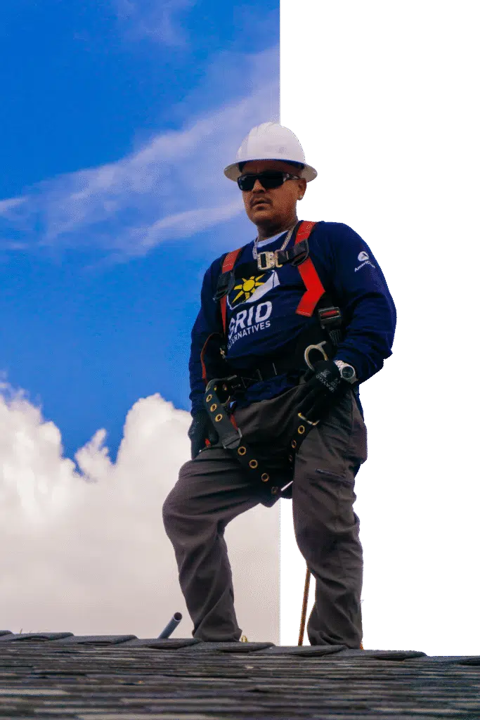 Worker in safety harness and hard hat on roofing structure against blue sky