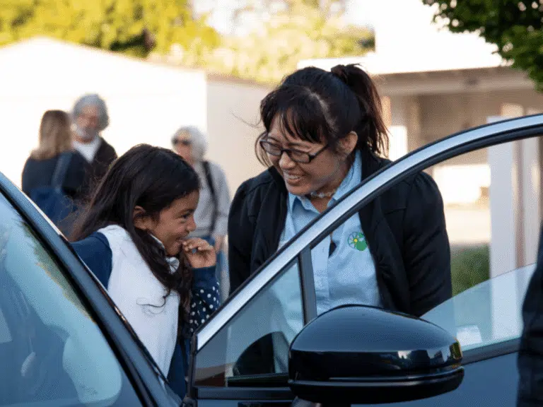 A GRID staff member laughs with a young girl beside an open car door.
