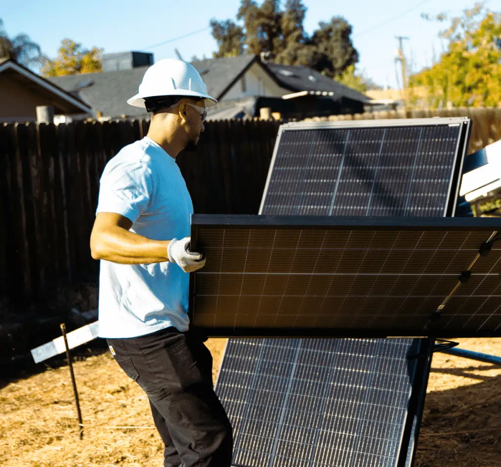 A man carries a battery storage unit across a yard toward a home.