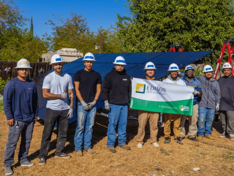 A GRID crew stands behind a completed ground-mount solar array holding an Edison International partnership banner.