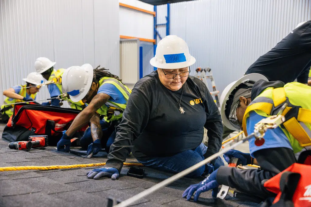 A group of trainees in hard hats and safety glasses gather around solar equipment in a workshop.