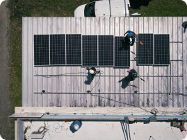 An aerial view of installers securing solar panels to a corrugated metal roof.
