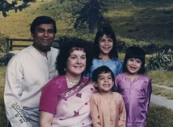 Family of five posing together outdoors with green hillside background