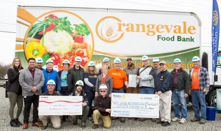 Group holding donation checks in front of Orangevale Food Bank truck with volunteers wearing white hard hats