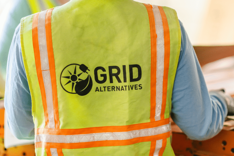 The back of a high-visibility safety vest printed with the GRID Alternatives sun-and-leaf logo.