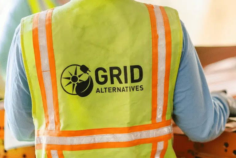 The back of a high-visibility safety vest printed with the GRID Alternatives sun-and-leaf logo.