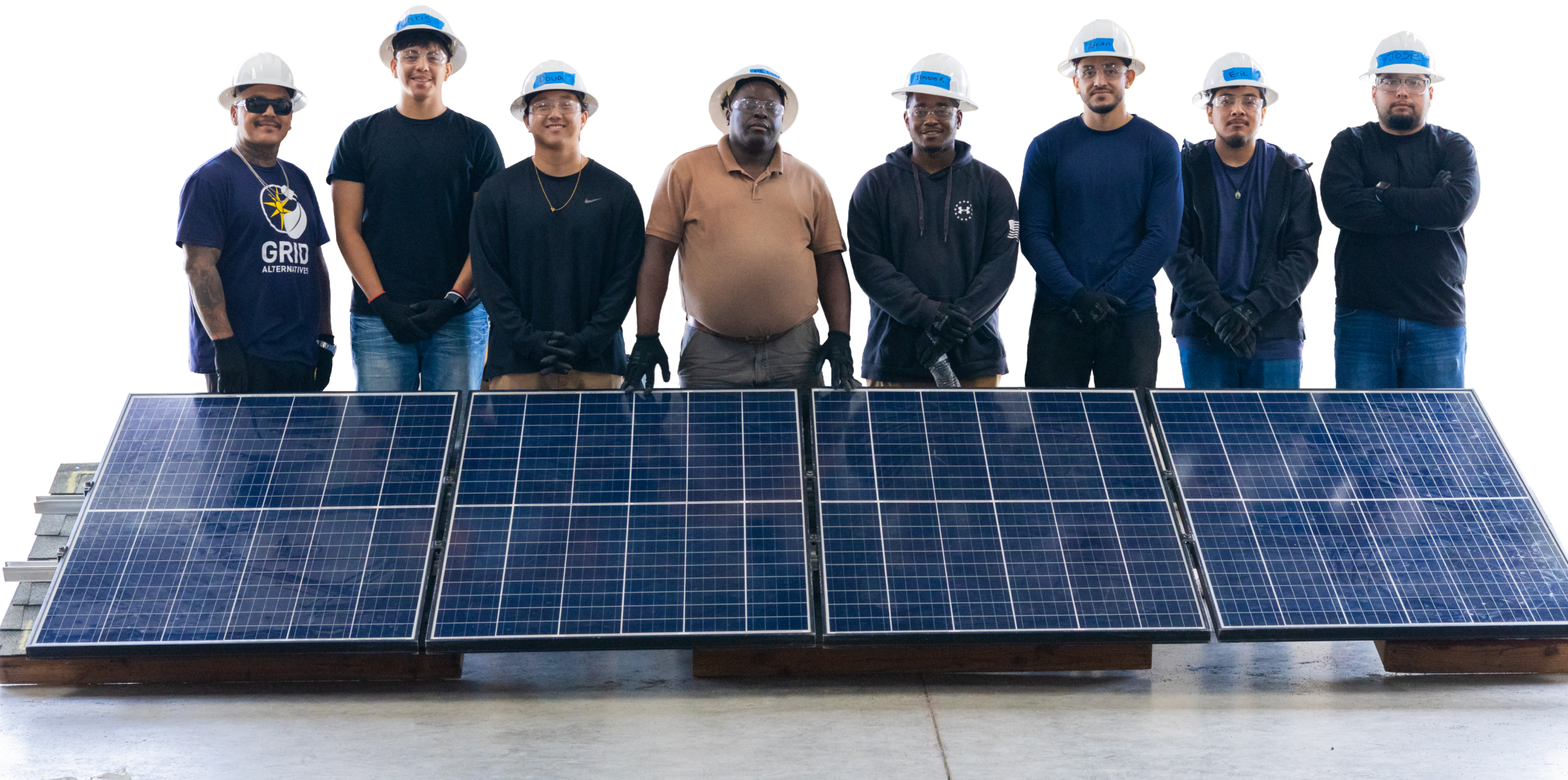 Eight people in hard hats and work clothes standing shoulder to shoulder behind a row of solar panels laid flat on the ground.