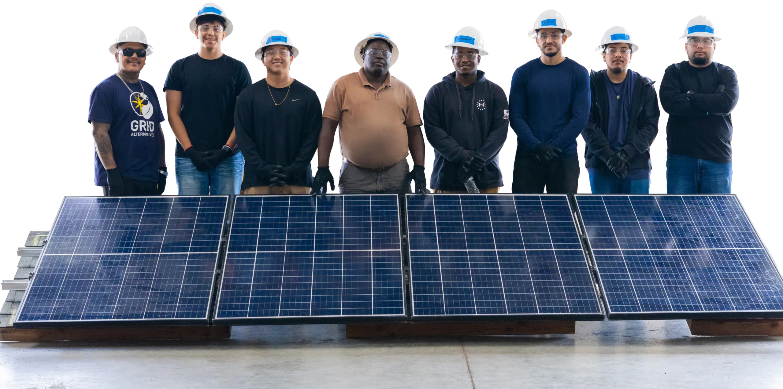 Eight people in hard hats and work clothes standing shoulder to shoulder behind a row of solar panels laid flat on the ground.