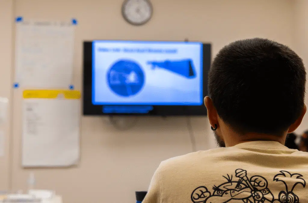 A person seen from behind watching a presentation slide on a wall-mounted screen in a meeting room.
