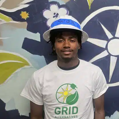 Man wearing white GRID Alternatives t-shirt and blue-white striped cap against floral backdrop