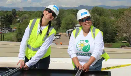 Two female Sunrun volunteers installing a solar panel on the roof.