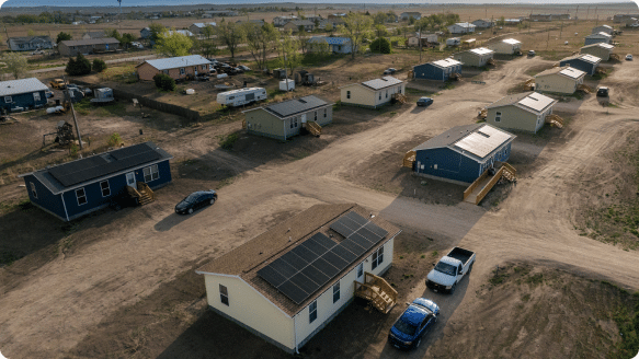 An aerial view of a rural neighborhood of small homes, one with rooftop solar panels installed in the foreground.