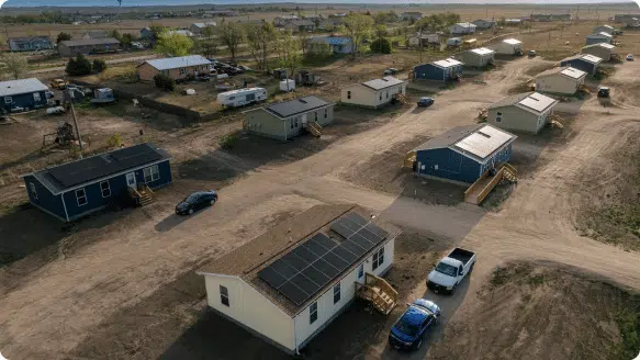 An aerial view of a rural neighborhood of small homes, one with rooftop solar panels installed in the foreground.