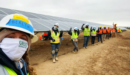 Worker in hard hat and mask at solar farm construction site with team in background