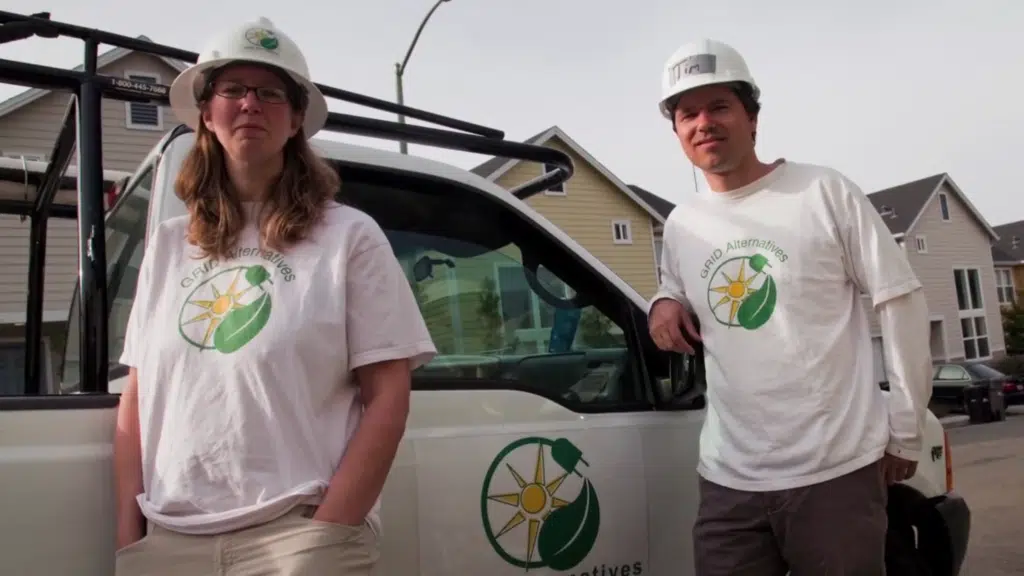 GRID Alternatives co-founders Erica Mackie and Tim Sears in hard hats and GRID Alternatives t-shirts, standing beside a company truck.