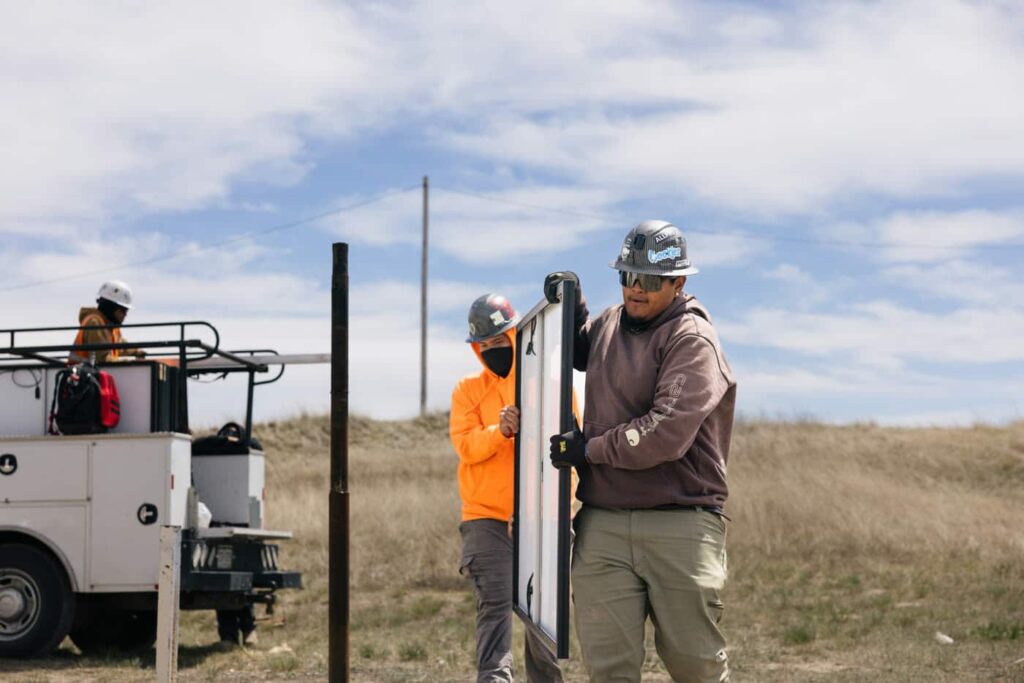 Three workers installing utility poles in a rural landscape with a service truck nearby