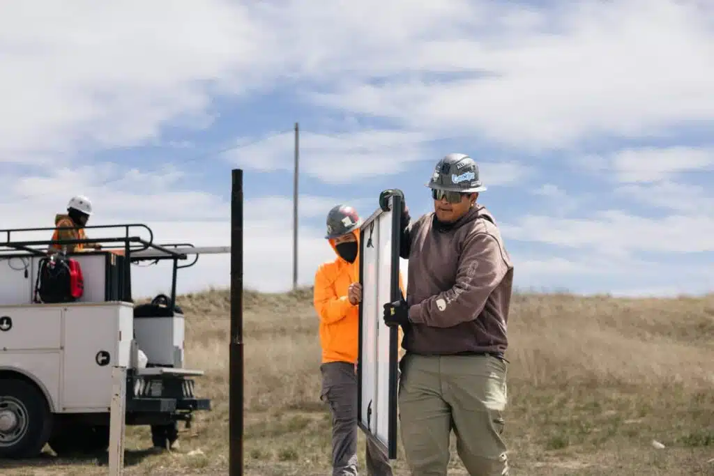 Three workers installing utility poles in a rural landscape with a service truck nearby