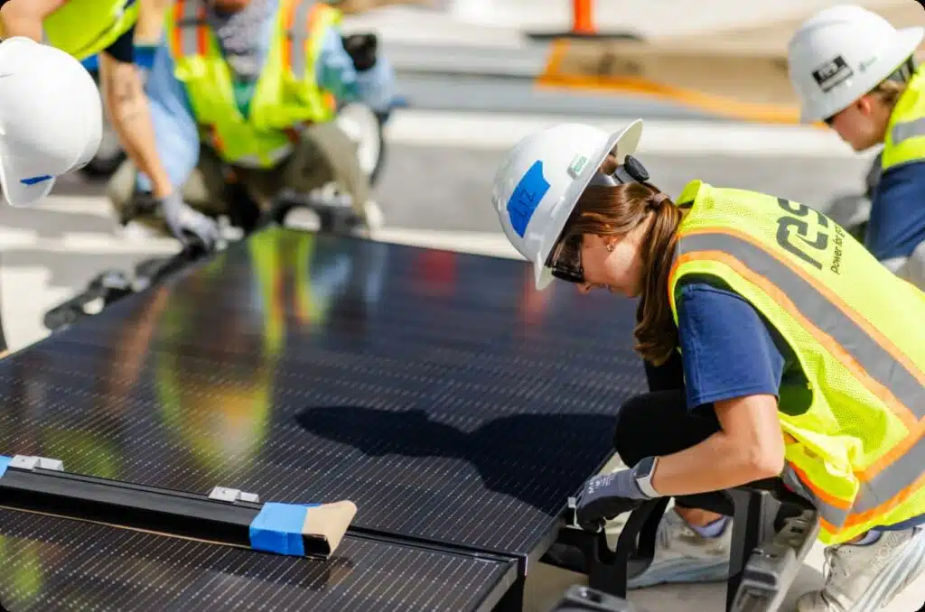 Workers in safety gear installing solar panels on rooftop
