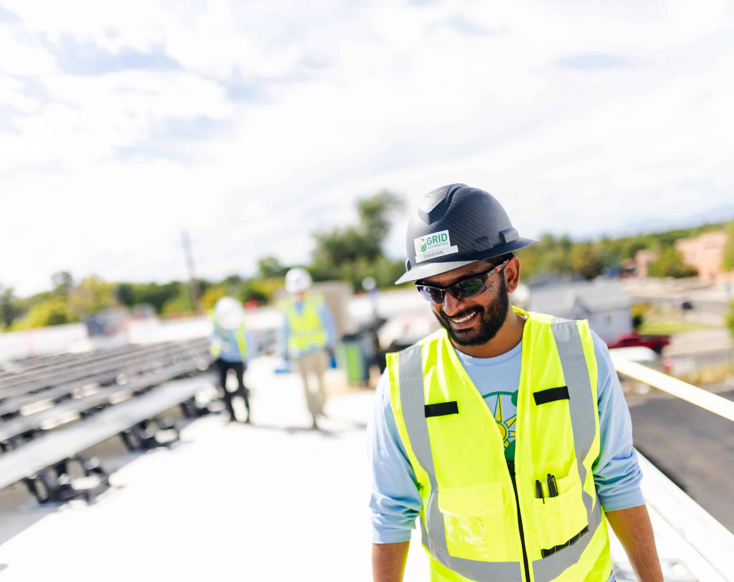 Construction worker on rooftop wearing safety gear and GRID vest smiling at camera