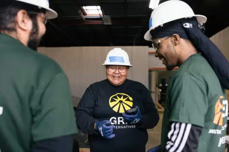 Three workers in hard hats and safety gear discuss at an industrial facility, representing volunteer or community involvement