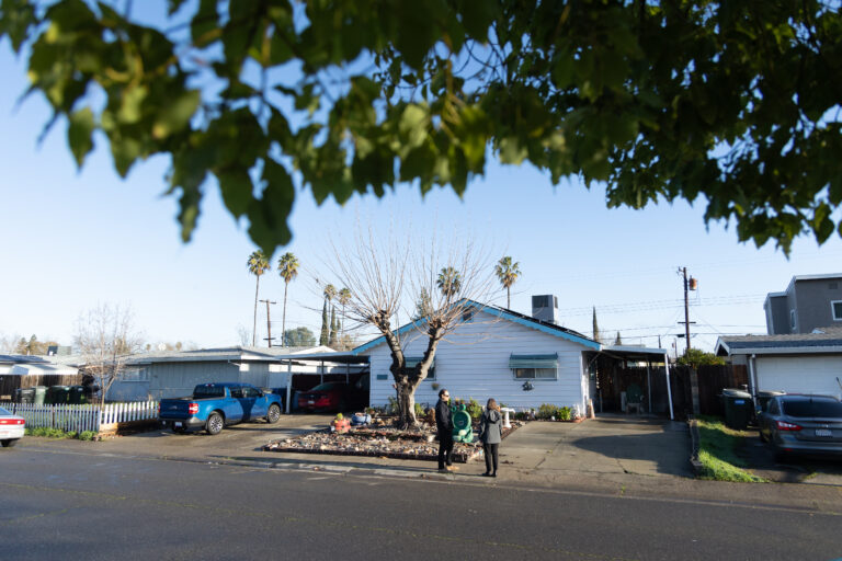 Two people talk in the front yard of homeowner Kathy Bigler's single-story home in Sacramento.