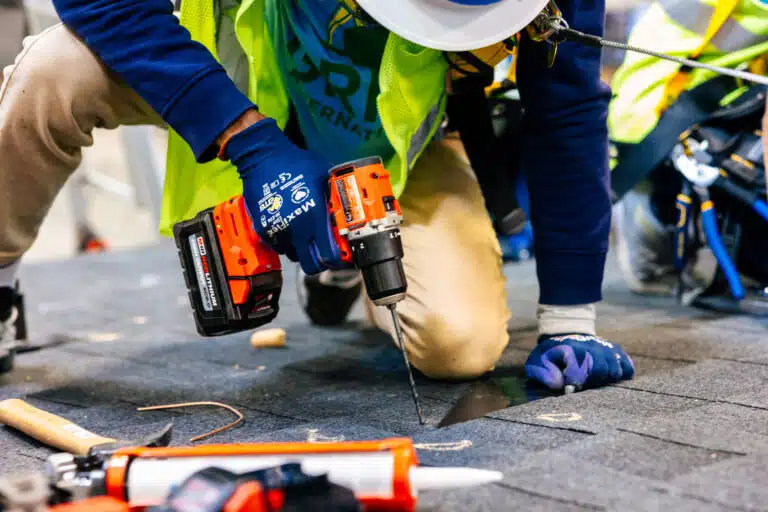Construction worker in safety gear using cordless drill on roofing material during training