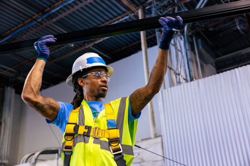 Construction worker in safety gear lifting steel beam overhead indoors