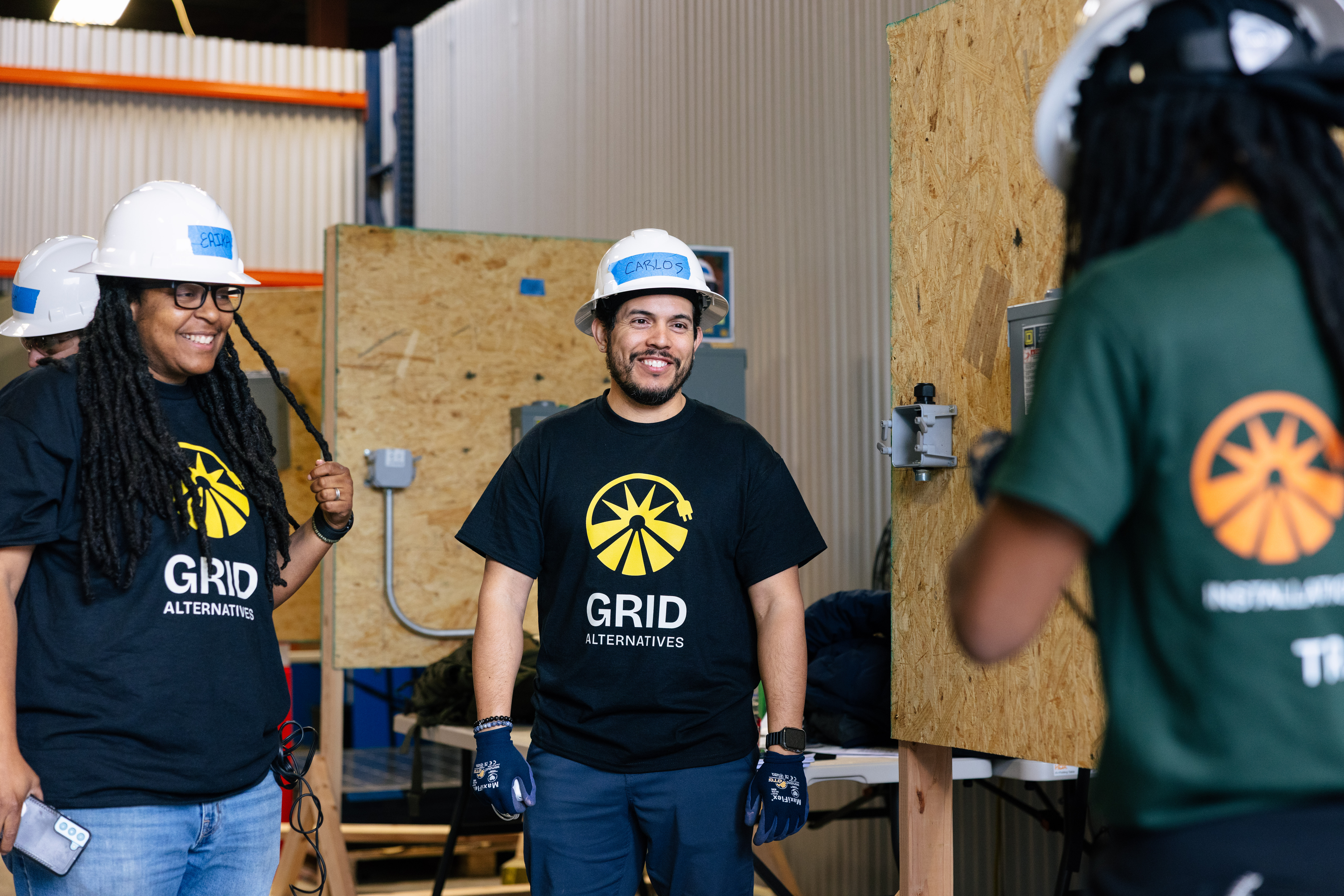 GRID Alternatives workers in hard hats and branded shirts during construction training inside a warehouse