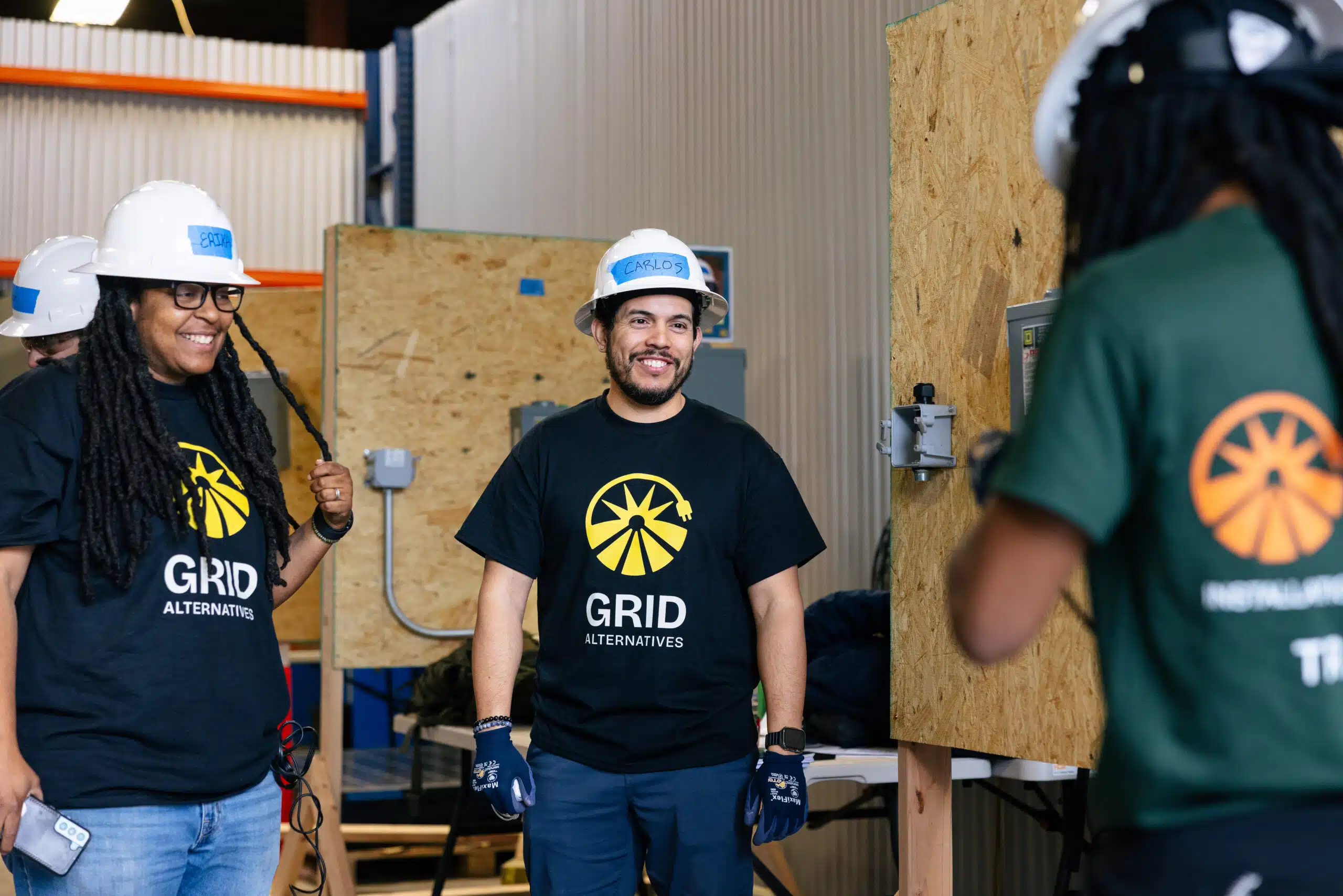 GRID Alternatives workers in hard hats and branded shirts during construction training inside a warehouse