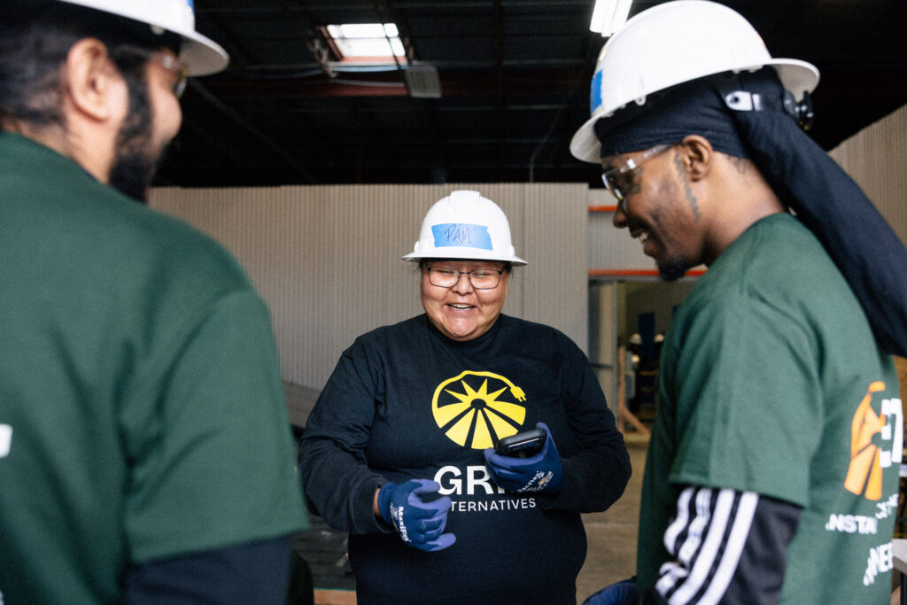 Three construction workers in hard hats and safety gear discuss a project in an industrial warehouse setting