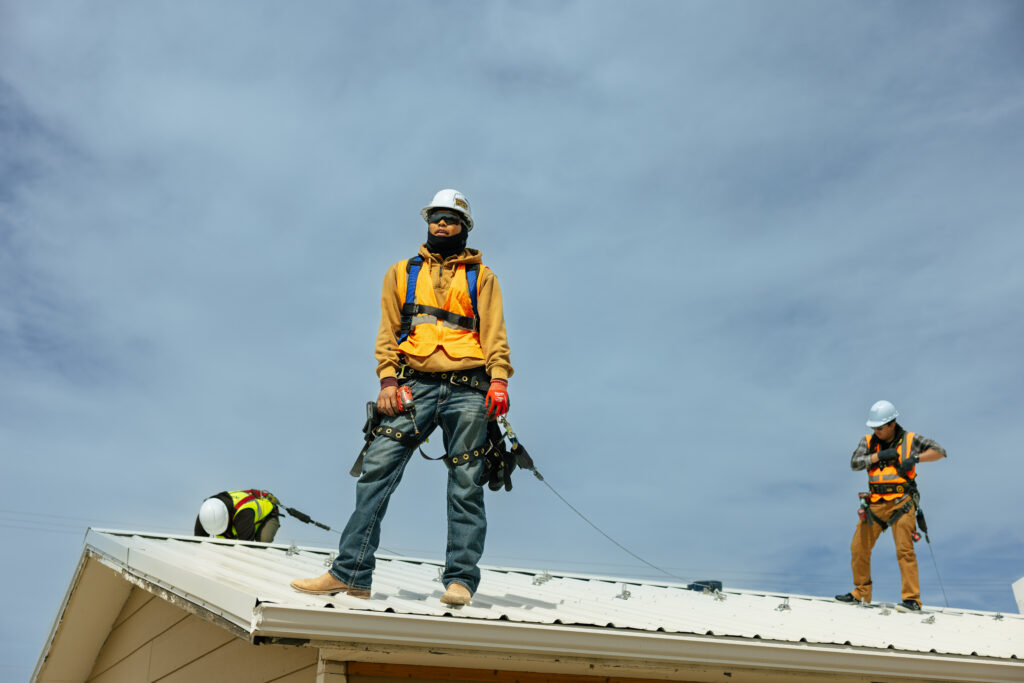 Construction workers in safety gear installing roofing on a residential building under blue sky