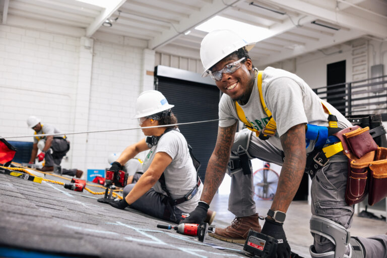 Two construction workers installing roofing material on an industrial building during a training program