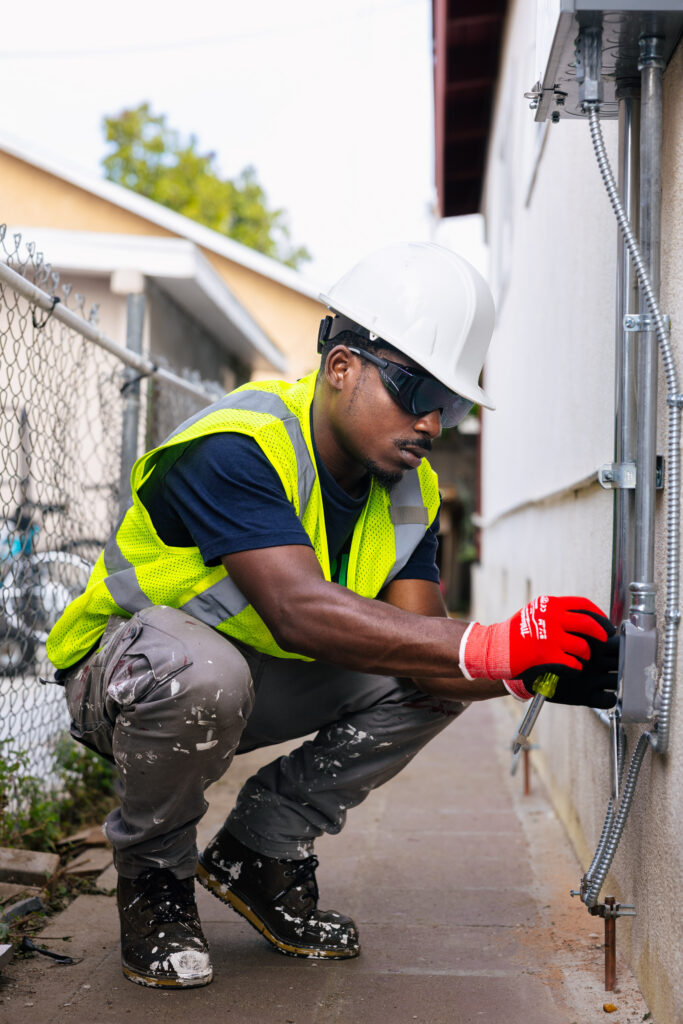 Construction worker in safety gear installing electrical equipment on residential wall