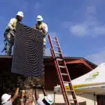 Workers installing solar panel on residential roof with ladder and safety equipment