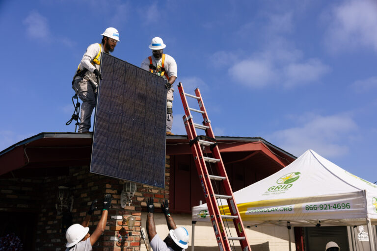 Workers installing solar panel on residential roof with ladder and safety equipment