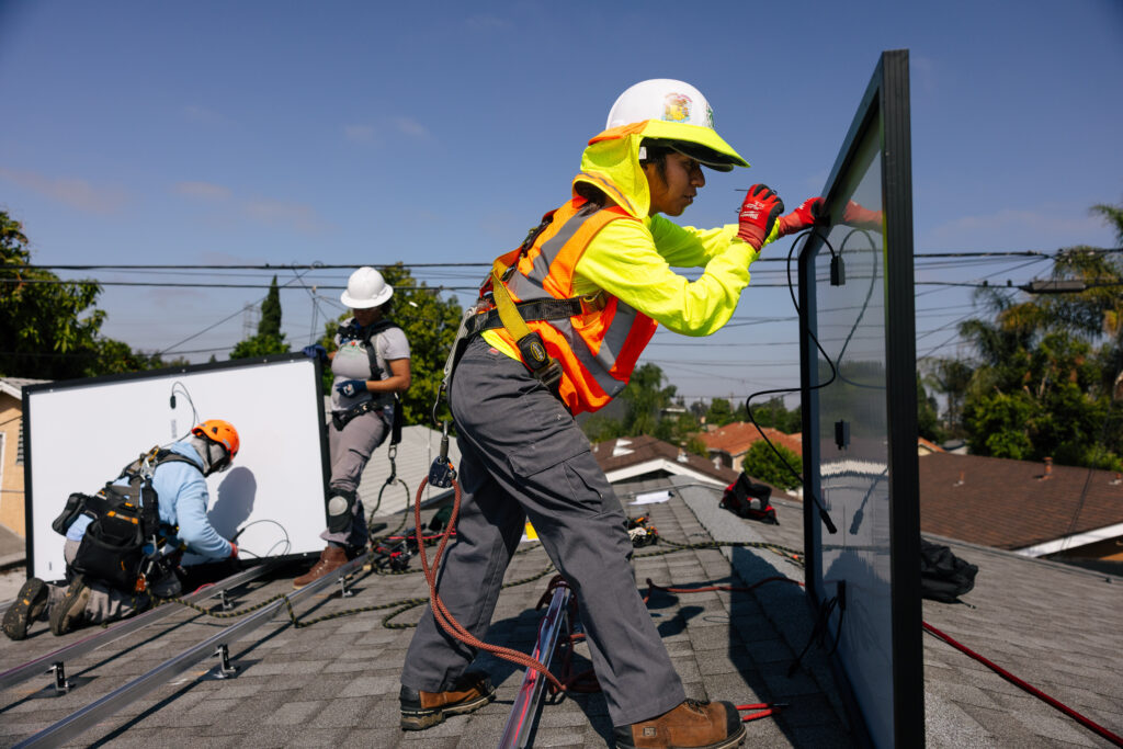 Workers installing solar panels on residential rooftop with safety equipment and harnesses