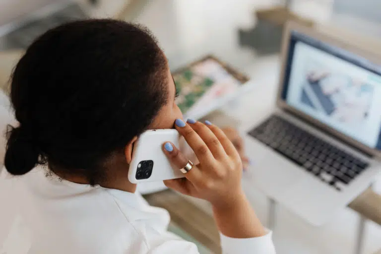 Person holding smartphone at desk with laptop, taking a call or video chat