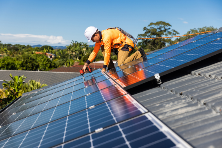 Solar technician in safety gear installing blue photovoltaic panels on residential roof