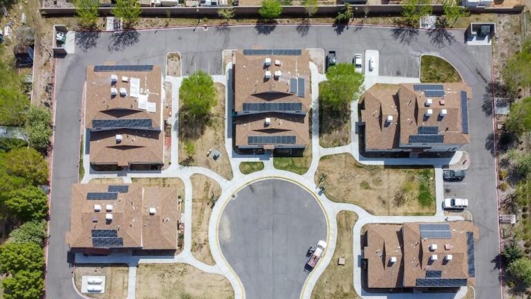 Aerial view of residential neighborhood with six brown-roofed houses arranged around a central circular cul-de-sac with solar panels on roofs