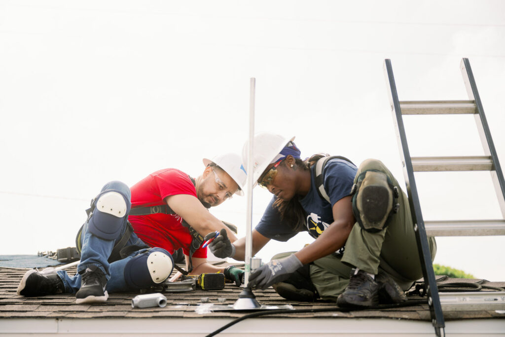 Two workers installing roofing materials on a residential roof with ladder visible