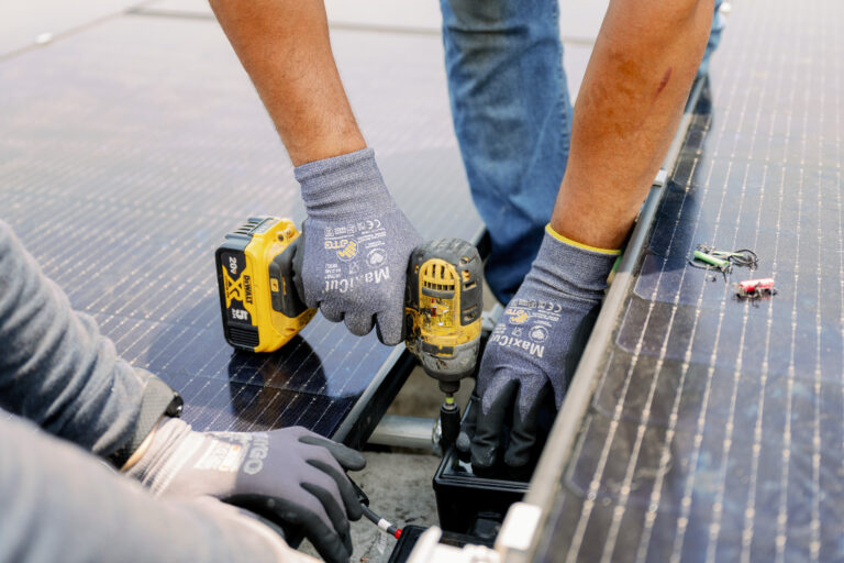 Workers installing solar panels on a roof with power tools and protective gloves