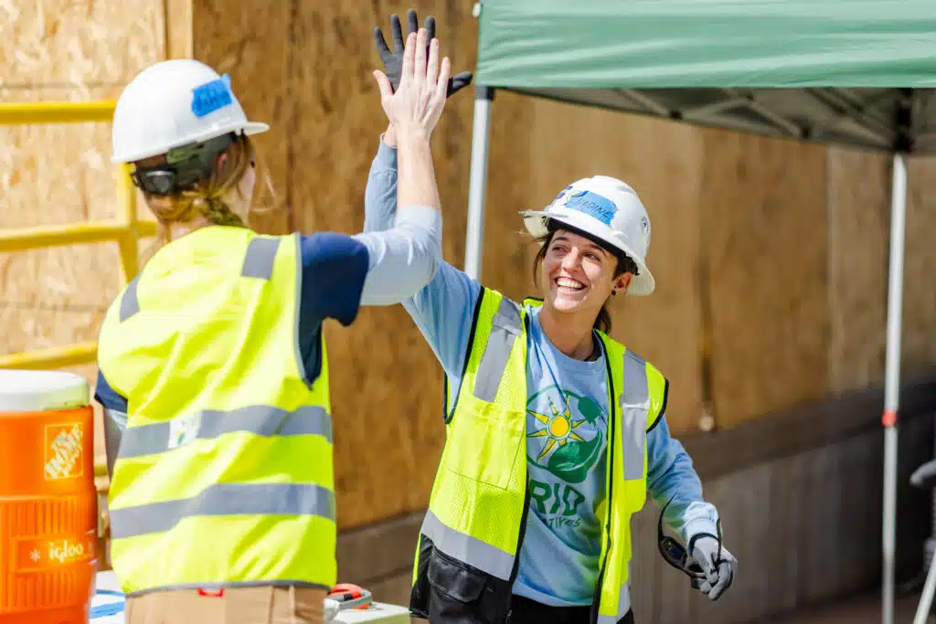 Two construction workers in safety vests and hard hats high-fiving at a job site