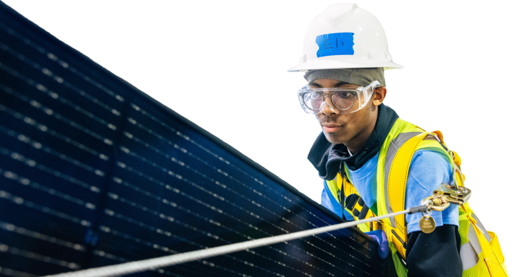 Worker in safety gear holding solar panel cable against dark panel