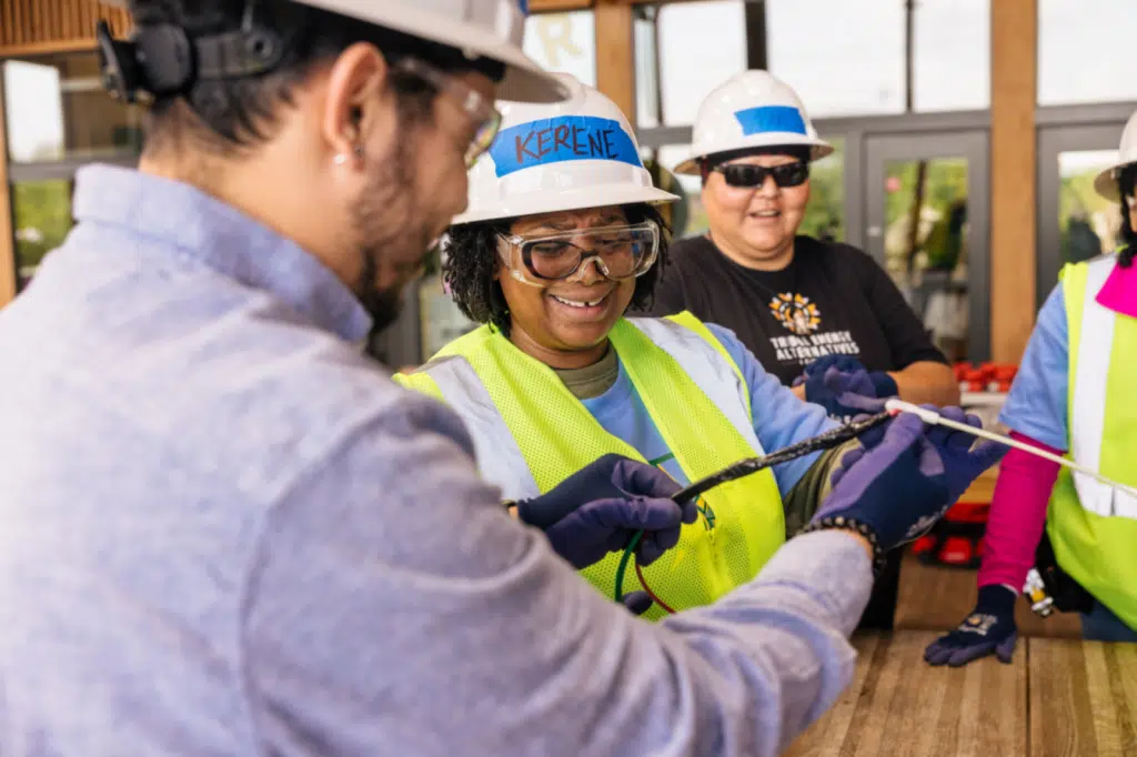 Two IBT trainees in hard hats and safety vests work together on a rooftop solar array
