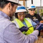 Two IBT trainees in hard hats and safety vests work together on a rooftop solar array