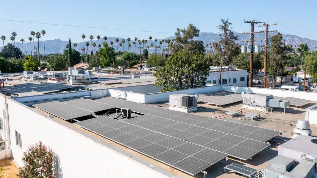 Rooftop solar panel array on white building with mountains and palm trees in background