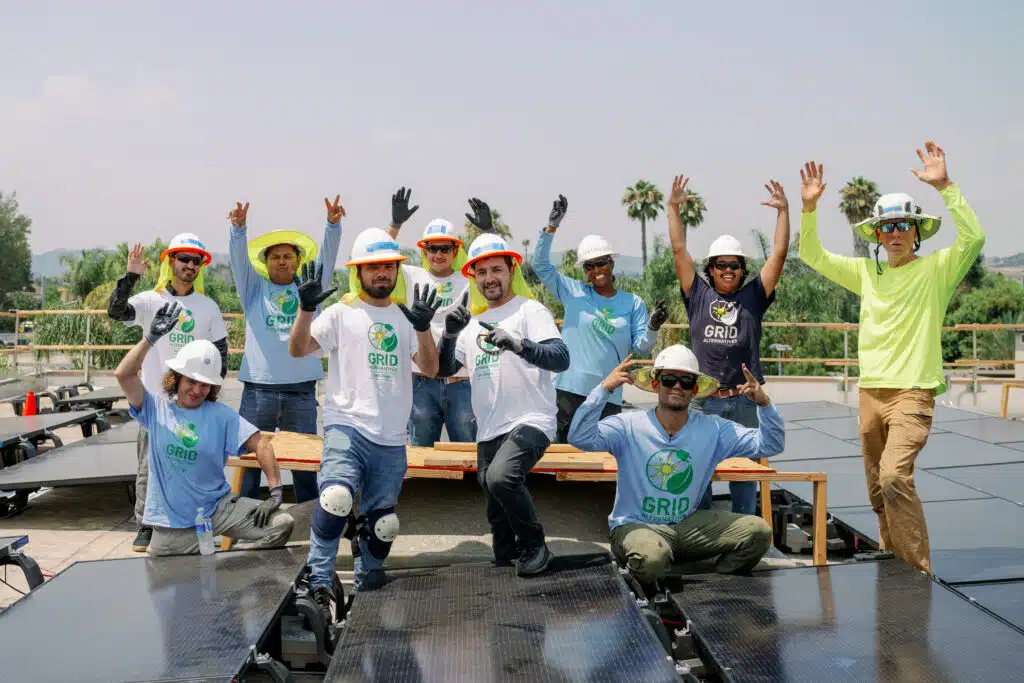 Team celebrates on solar panel installation, wearing GRID branded shirts and hard hats
