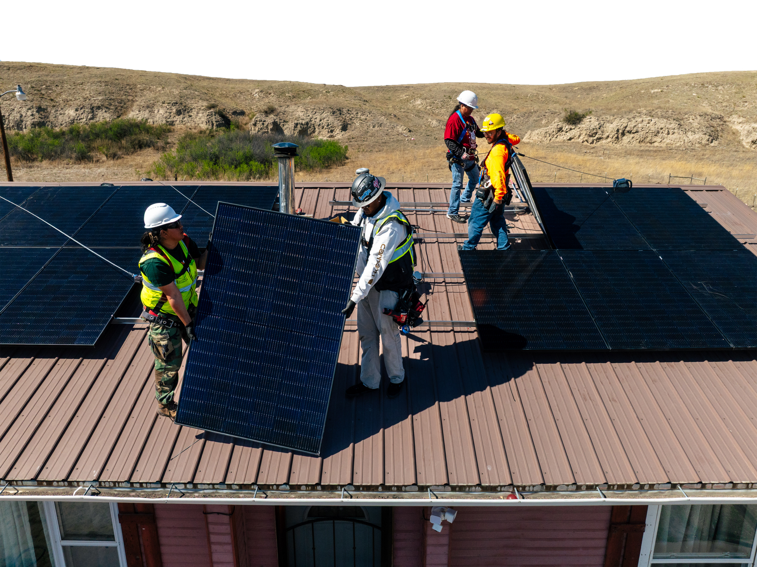 Workers in safety gear install solar panels on a residential roof against a hillside backdrop