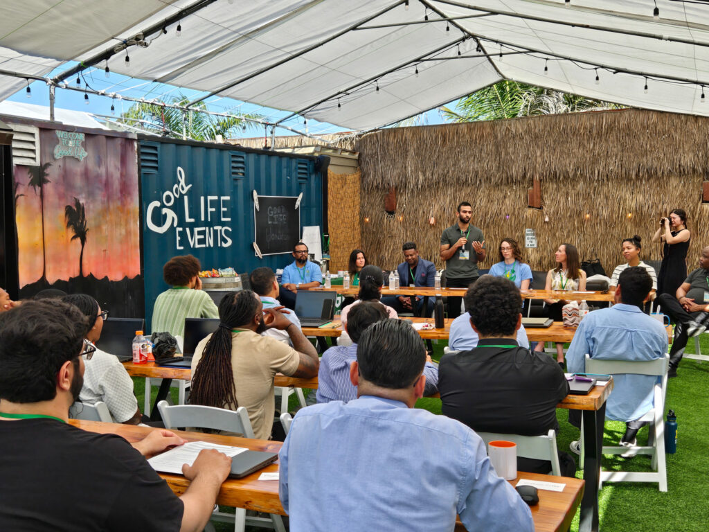 Panel discussion at Good Life Events outdoor venue with diverse audience seated at tables under shade structures